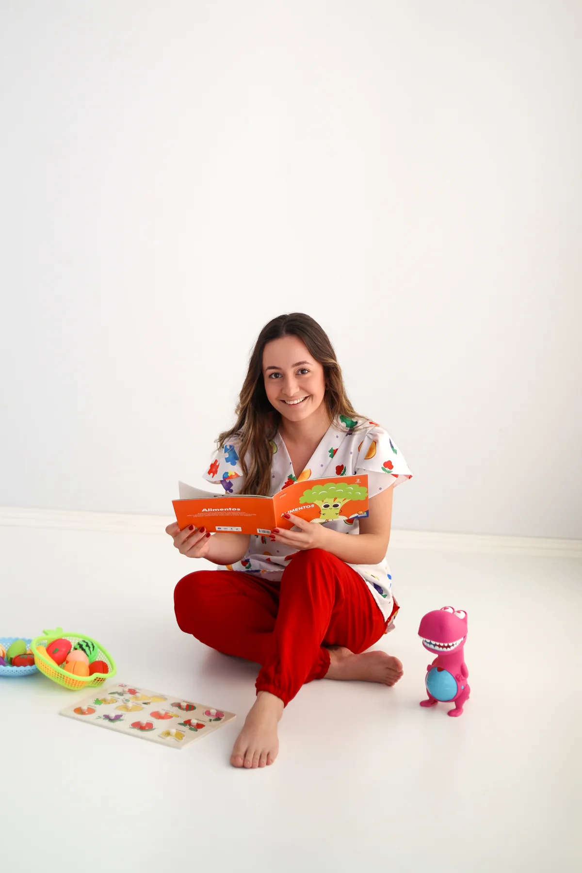 Laura sentada no chão com livros e brinquedos educativos.