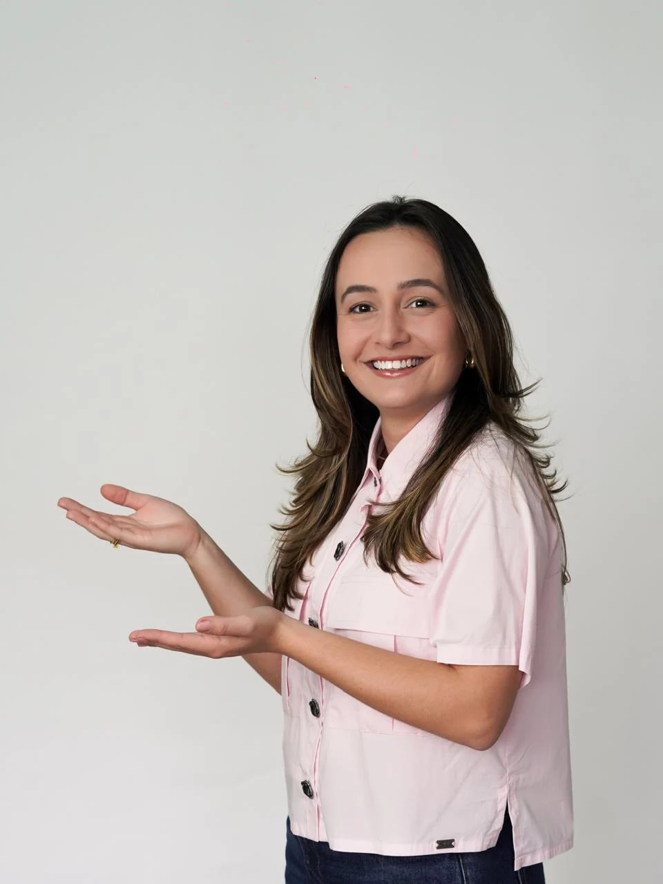 Laura de camisa rosa, sorrindo e apresentando com as m?os abertas.